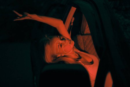 Foto de Una hermosa chica de aspecto europeo se sienta en el asiento del pasajero en el coche y mirando a la ventana - Imagen libre de derechos