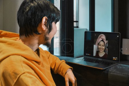 Téléchargez les photos : Un Asiatique est assis dans un petit bureau et communique par liaison vidéo via un ordinateur portable avec sa petite amie. Le concept de communication en ligne, quarantaine, distance. - en image libre de droit