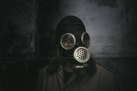Foto de Un hombre con una máscara de gas que permanece en la oscuridad en un edificio en ruinas, cubierta de libro - Imagen libre de derechos