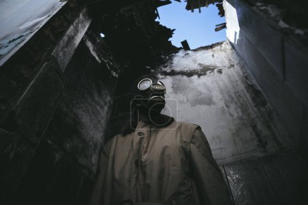 Photo for A man wearing a gas mask inside a ruined building with a leaky roof in the dark, apocalypse, good for book cover, low angle - Royalty Free Image
