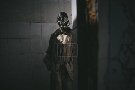 Foto de Un hombre con máscara de gas de pie dentro de un edificio viejo, mirando a la vuelta de la esquina, bueno para la portada del libro - Imagen libre de derechos
