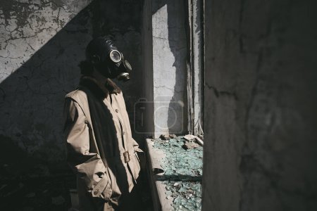 Téléchargez les photos : Une personne portant un masque à gaz est debout devant la fenêtre d'une maison détruite, bon pour la couverture du livre - en image libre de droit