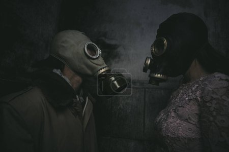 Téléchargez les photos : Deux personnes dans des masques à gaz se tiennent contre un mur dans une petite pièce sombre et se regardent, gros plan, bon pour la couverture du livre - en image libre de droit