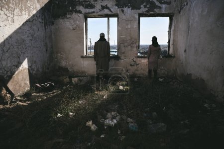 Photo for Two people, a guy and a girl in gas masks, stand inside an abandoned house next to the window and look forward, apocalypse - Royalty Free Image