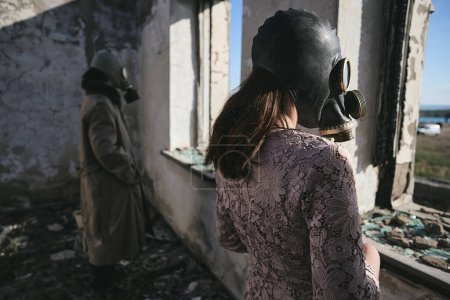 Foto de Una mujer y un hombre con una máscara de gas están en un edificio abandonado y miran por la ventana - Imagen libre de derechos