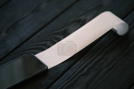 Téléchargez les photos : Un téléphone portable avec un chèque en blanc sur une table en bois noir, concept financier - en image libre de droit