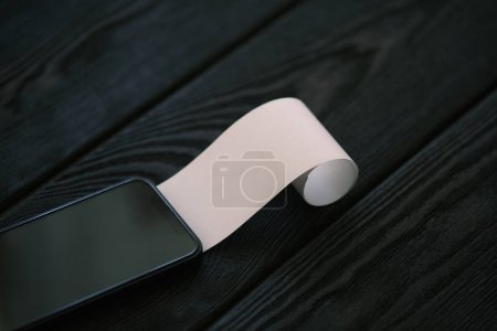 Téléchargez les photos : Un téléphone portable avec un chèque en blanc sur une table en bois noir, concept financier - en image libre de droit