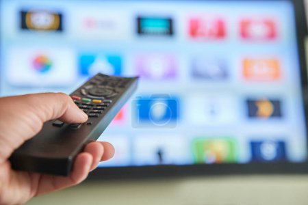 Photo for Multimedia streaming concept. Hand holding remote control. TV screen with lot of pictures. - Royalty Free Image