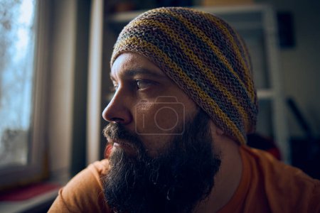 Photo for A man with a beard wearing a striped hat and t-shirt, looking up into the window - Royalty Free Image