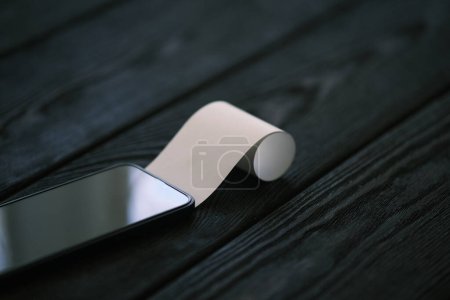 Foto de Un teléfono móvil con un cheque en blanco en la mesa de madera negro, concepto financiero - Imagen libre de derechos