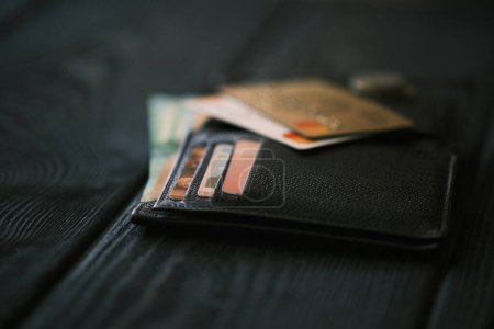 Foto de Un teléfono móvil que pone en un bolso de cuero y una pequeña pila de monedas en la mesa de madera negro, concepto financiero - Imagen libre de derechos