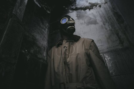 Téléchargez les photos : Un homme portant un masque à gaz à l'intérieur d'un bâtiment en ruine avec un toit qui fuit dans l'obscurité, apocalypse, bon pour la couverture du livre, angle bas - en image libre de droit