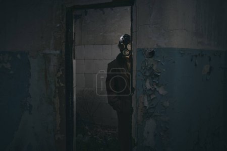 Foto de Un hombre con máscara de gas de pie dentro de un edificio viejo, mirando a la vuelta de la esquina, bueno para la portada del libro - Imagen libre de derechos