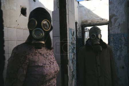 Téléchargez les photos : La femme dans un masque à gaz restant devant un homme dans un bâtiment détruit, bon pour la couverture du livre - en image libre de droit
