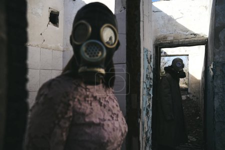 Téléchargez les photos : La femme dans un masque à gaz restant devant un homme dans un bâtiment détruit, bon pour la couverture du livre - en image libre de droit