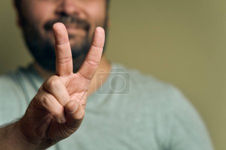 Téléchargez les photos : Un homme barbu européen montre la victoire signe de la main - en image libre de droit