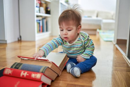 Photo for Cute baby sitting and looking at a large book. - Royalty Free Image