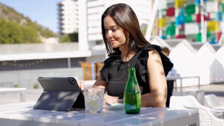Una mujer elegante está utilizando una tableta en una mesa de café al aire libre con una bebida refrescante en España.