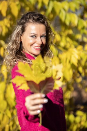 Beautiful smiling woman outdoor portrait holding a leaf in front of the camera.