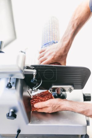 Italian chef slicing ham for pizza in restaurant kitchen on slicing machine