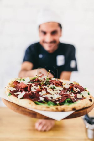 Smiling Italian chef or pizzaiolo offering pizza in restaurant