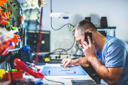 Man speaking on mobile phone while repairing electronics in service and maintenance shop
