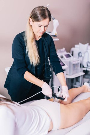 Woman, a beautician doing radiofrequency RF treatment on her client's thigh in a beauty salon. Skin tightening, body contouring, and reducing wrinkles.