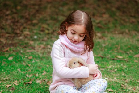 Foto de Happy little girl with a rabbit in her hands in the park - Imagen libre de derechos