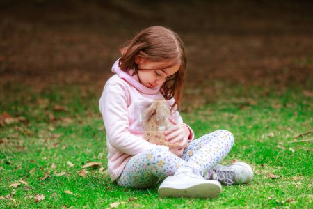 Foto de Happy little girl with a rabbit in her hands in the park - Imagen libre de derechos