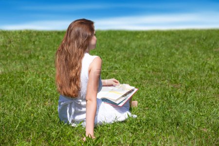 Téléchargez les photos : Happy female student sitting on the grass with a book - en image libre de droit