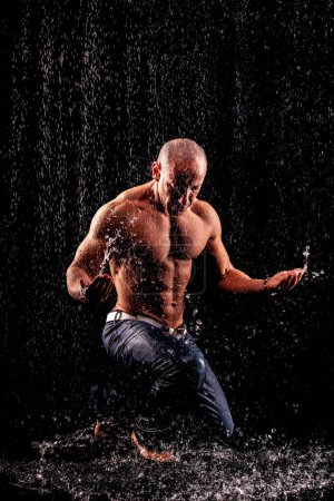 Photo for Athlete bodybuilder under jets of rain on a black background - Royalty Free Image