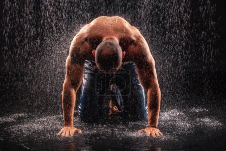 Photo for Athlete bodybuilder under jets of rain on a black background - Royalty Free Image