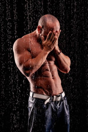 Téléchargez les photos : Bodybuilder athlète sous des jets de pluie sur un fond noir - en image libre de droit