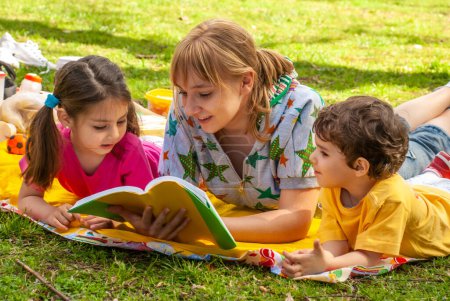 Téléchargez les photos : Joyeux famille dans le parc sur l'herbe en lisant un livre - en image libre de droit
