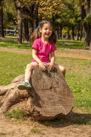 Foto de Niña alegre sentada en un árbol en el parque - Imagen libre de derechos