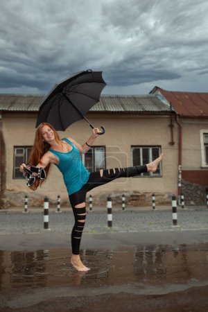 Téléchargez les photos : Heureuse jeune fille avec parapluie dansant dans une flaque - en image libre de droit