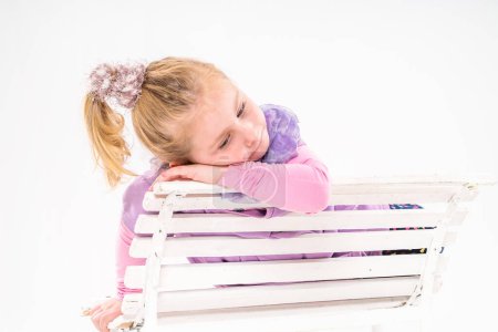 Téléchargez les photos : Triste petite fille assise sur un banc sur un fond clair - en image libre de droit