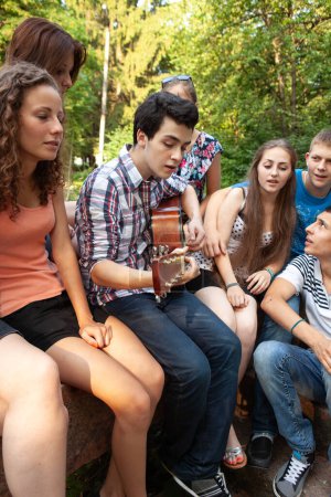 Foto de Grupo de jóvenes relajándose en el parque con una guitarra - Imagen libre de derechos