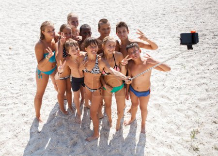 Téléchargez les photos : Un groupe joyeux d'enfants sur une plage de sable prenant un selfie - en image libre de droit