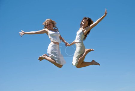 Téléchargez les photos : Filles heureuses sautant contre le ciel - en image libre de droit