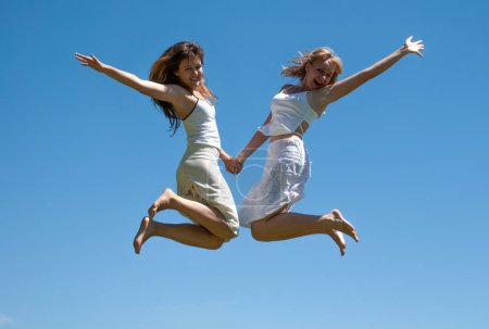 Téléchargez les photos : Filles heureuses sautant contre le ciel - en image libre de droit