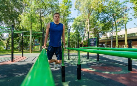 Téléchargez les photos : Jeune athlète homme faisant de l'exercice sur des équipements sportifs dans le parc - en image libre de droit