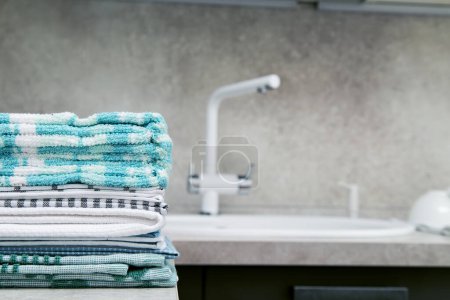 Téléchargez les photos : Les serviettes de cuisine sont empilées sur la table de cuisine à côté de l'évier et du robinet. Espace pour le texte. - en image libre de droit