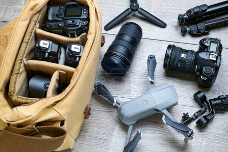 Professional photography equipment, drone, tripod and canvas bag on gray table. View from above.