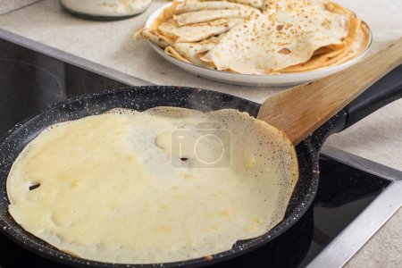 Photo for Delicious thin pancakes on a non-stick pan. cooking process.  A wooden spatula flips the pancake. - Royalty Free Image