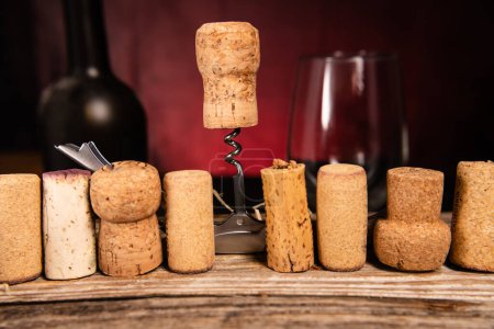 Sommelier knife and wine cork close-up on the background of used corks on a wooden table. Red blurred background. Space for text.