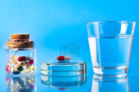 Foto de Píldora y un vaso de agua en una mesa azul vidriosa. Reflexión en vidrio. Primer plano. Espacio para el texto. El concepto de tratamiento y salud. - Imagen libre de derechos