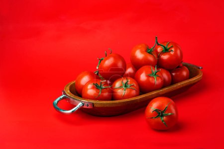 Téléchargez les photos : Tomates fraîches mûres dans un bol en bois sur fond rouge. - en image libre de droit
