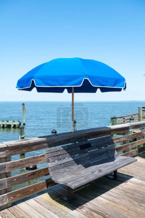 Photo for Memorial bench with umbrella with bronze plaque on a wooden pleasure pier on the shores of the Atlantic Ocean. - Royalty Free Image