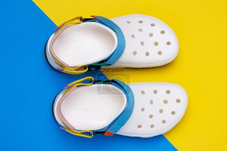 Photo for White Croc slippers with straps on a yellow and blue background. Comfortable unisex beach shoes. - Royalty Free Image